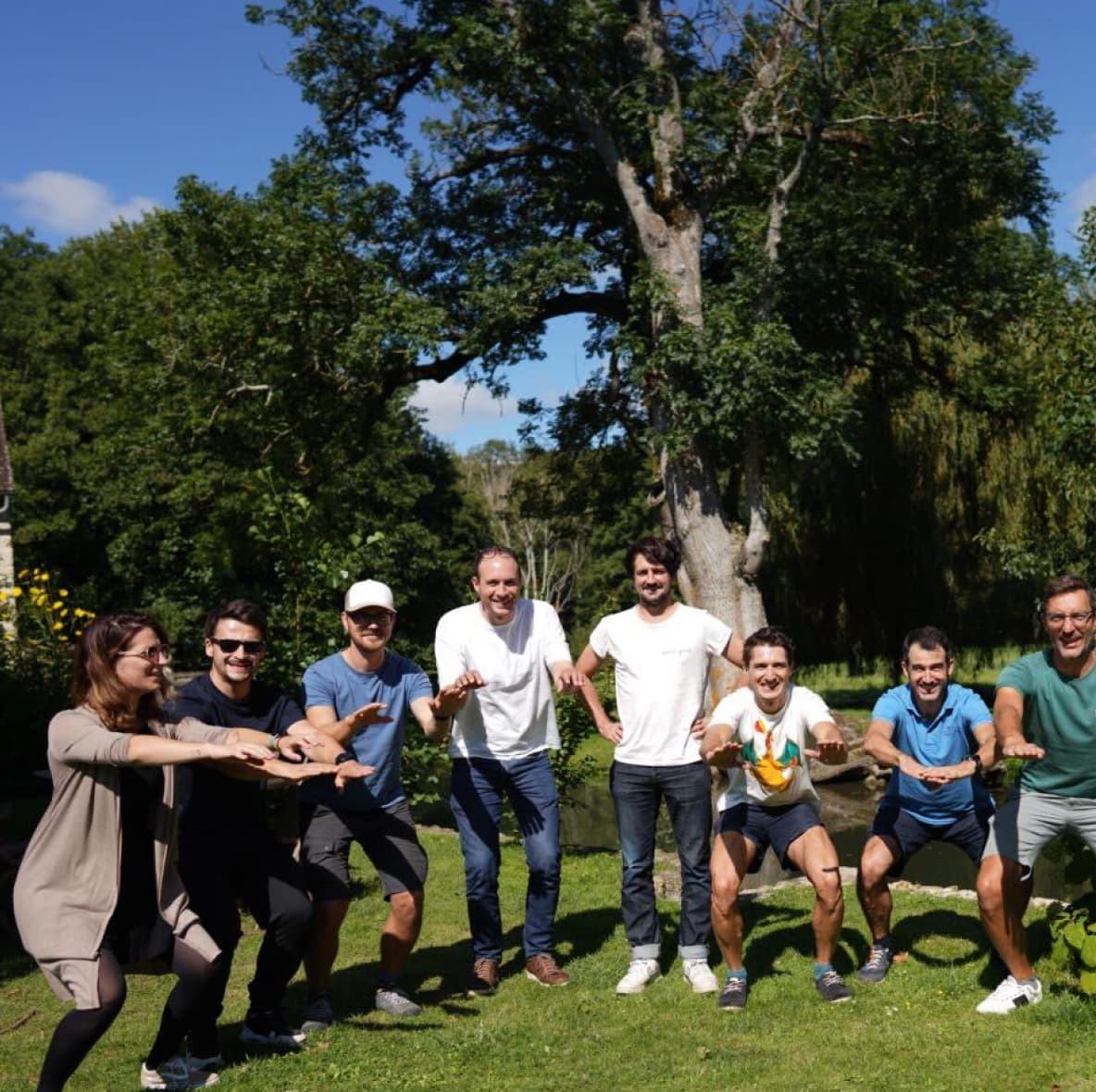 L'équipe Claap réunie sur une pelouse devant un grand arbre, les bras tendus en plein clap.